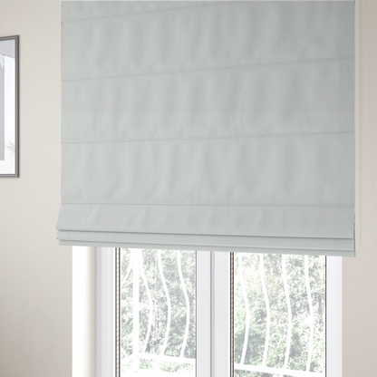 The fabric used to create these Roman blinds is a solid, off-white or light cream-coloured woven fabric. The weave appears consistent and fine, creating a subtle, clean aesthetic.