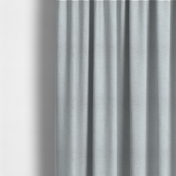 The fabric used to create these made-to-measure curtains is a cool-toned, light grey or silver upholstery fabric. It showcases the same dense, uniform, boucle-style weave seen in the previous image, consisting of small, looped, and nubby yarn fibres that create a soft, tactile surface.