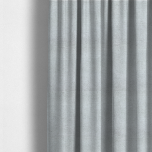The fabric used to create these made-to-measure curtains is a cool-toned, light grey or silver upholstery fabric. It showcases the same dense, uniform, boucle-style weave seen in the previous image, consisting of small, looped, and nubby yarn fibres that create a soft, tactile surface.