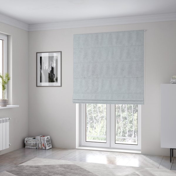 The fabric used to create these Roman blinds is a cool-toned, light grey or silver upholstery fabric. It showcases the same dense, uniform, boucle-style weave seen in the previous image, consisting of small, looped, and nubby yarn fibres that create a soft, tactile surface.