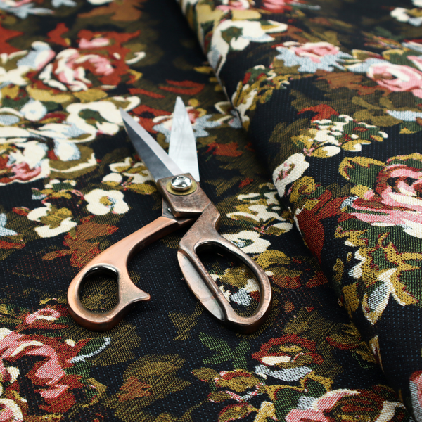A repeating vintage floral pattern on a dark black and olive green woven fabric background. The pattern features clusters of blooming roses in shades of dusty pink, burgundy, cream, and muted light blue, accompanied by small accent flowers and olive green leaves.   