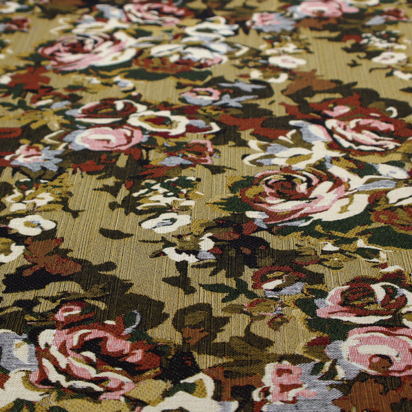 A repeating vintage floral pattern on a warm gold and beige textured woven fabric background. The design features dense clusters of blooming roses in shades of dusty pink, deep red, cream, and muted lavender, surrounded by olive green and dark foliage.   