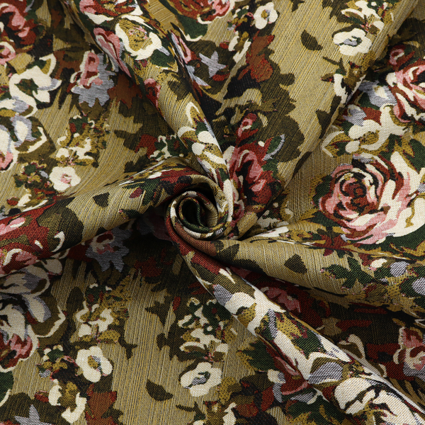 A repeating vintage floral pattern on a warm gold and beige textured woven fabric background. The design features dense clusters of blooming roses in shades of dusty pink, deep red, cream, and muted lavender, surrounded by olive green and dark foliage.   