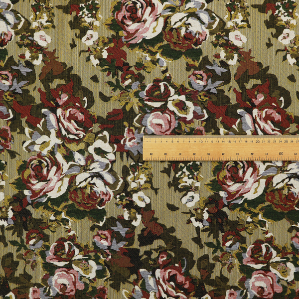 A repeating vintage floral pattern on a warm gold and beige textured woven fabric background. The design features dense clusters of blooming roses in shades of dusty pink, deep red, cream, and muted lavender, surrounded by olive green and dark foliage.   