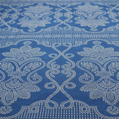 An ornate, traditional damask upholstery fabric on a rich blue background featuring intricate cream-coloured symmetrical floral and paisley motifs divided horizontally by a decorative lattice and scroll border.   