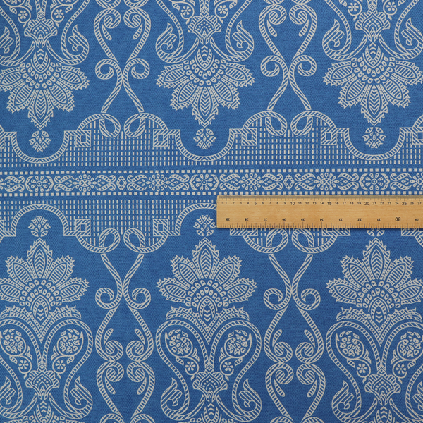 An ornate, traditional damask upholstery fabric on a rich blue background featuring intricate cream-coloured symmetrical floral and paisley motifs divided horizontally by a decorative lattice and scroll border.   