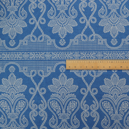 An ornate, traditional damask upholstery fabric on a rich blue background featuring intricate cream-coloured symmetrical floral and paisley motifs divided horizontally by a decorative lattice and scroll border.   