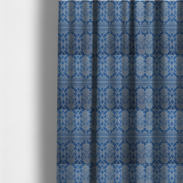 The fabric used to create these made-to-measure curtains is an ornate, traditional damask upholstery fabric on a rich blue background featuring intricate cream-coloured symmetrical floral and paisley motifs divided horizontally by a decorative lattice and scroll border.   