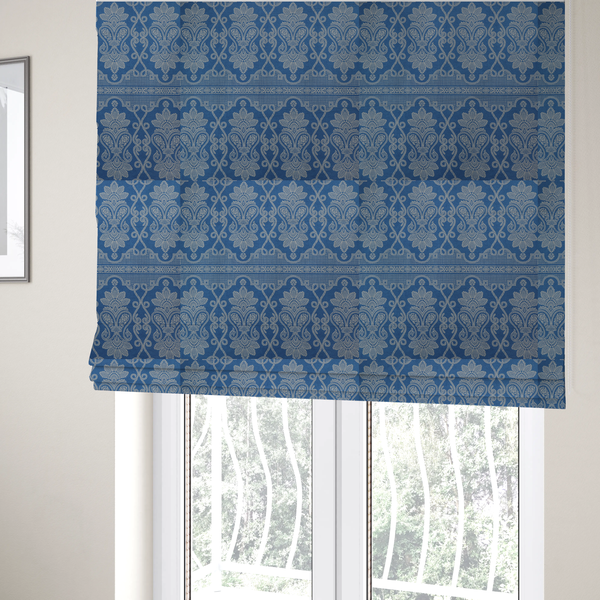 The fabric used to create these Roman blinds is a ornate, traditional damask upholstery fabric on a rich blue background featuring intricate cream-coloured symmetrical floral and paisley motifs divided horizontally by a decorative lattice and scroll border.   