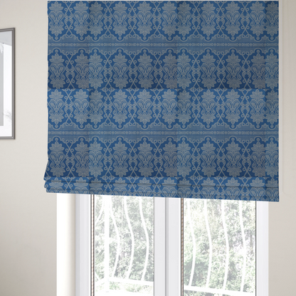 The fabric used to create these Roman blinds is a ornate, traditional damask upholstery fabric on a rich blue background featuring intricate cream-coloured symmetrical floral and paisley motifs divided horizontally by a decorative lattice and scroll border.   