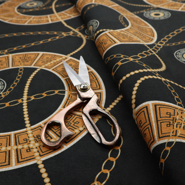A glamorous luxury-style upholstery fabric on a black background featuring a repeating pattern of large gold-and-white patterned circular rings interconnected by dangling gold chains and small black-and-white geometric medallions.   