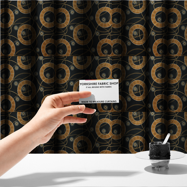 The fabric used to create these made-to-measure curtains is a glamorous luxury-style upholstery fabric on a black background featuring a repeating pattern of large gold-and-white patterned circular rings interconnected by dangling gold chains and small black-and-white geometric medallions.   