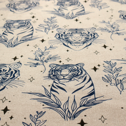 A seamless pattern fabric featuring line-drawn navy blue tigers, leafy botanical branches, and small sparkling star accents set against a light beige background.   