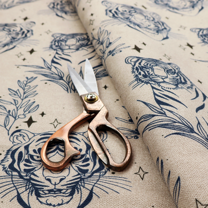 A seamless pattern fabric featuring line-drawn navy blue tigers, leafy botanical branches, and small sparkling star accents set against a light beige background.   