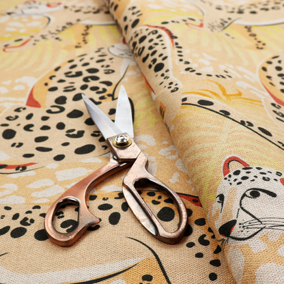 A playful patterned fabric featuring illustrated leopards in various poses with black spots and red-tipped ears, set against a warm yellow and beige jungle foliage background.   