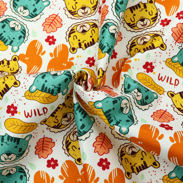 A playful cartoon fabric print on a light background featuring alternating yellow and turquoise tiger cub faces, orange cactus silhouettes, yellow leaves, red flower blossoms, and the word "WILD" written in red text.   