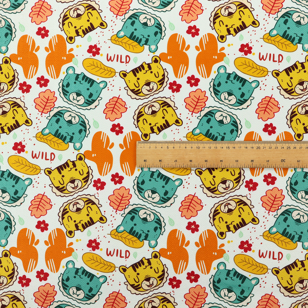 A playful cartoon fabric print on a light background featuring alternating yellow and turquoise tiger cub faces, orange cactus silhouettes, yellow leaves, red flower blossoms, and the word "WILD" written in red text.   