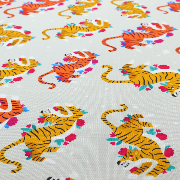 A playful patterned fabric featuring whimsical leaping tigers in shades of orange and yellow, accented with colourful floral elements on a light grey background.   