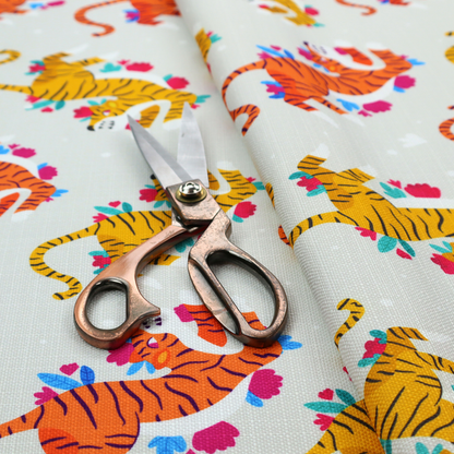 A playful patterned fabric featuring whimsical leaping tigers in shades of orange and yellow, accented with colourful floral elements on a light grey background.   