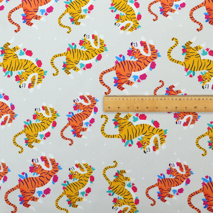 A playful patterned fabric featuring whimsical leaping tigers in shades of orange and yellow, accented with colourful floral elements on a light grey background.   