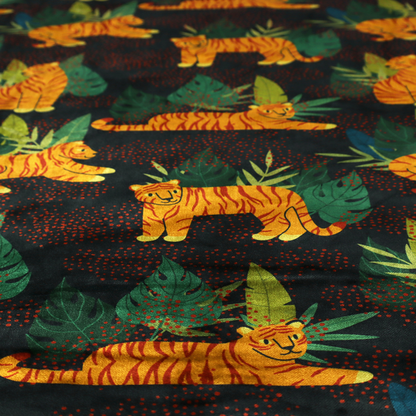 A vibrant fabric pattern featuring illustrated orange tigers in various poses surrounded by dark green tropical leaves and foliage against a dark background with red dotted accents.   
