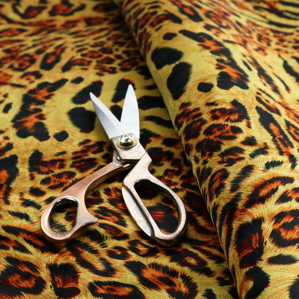A bold, symmetrical leopard print fabric featuring a repeating kaleidoscope pattern of black and golden-brown rosettes on a warm yellow-gold background.