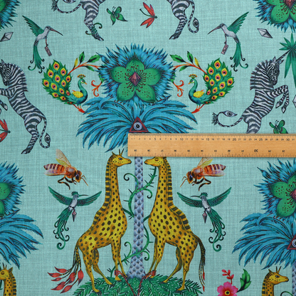 An enchanting turquoise-toned fabric pattern featuring zebras, giraffes, hummingbirds, peacocks, bees, and mystical blue flowers with eye motifs on a light aqua background.
