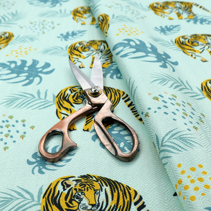 A tropical jungle upholstery fabric on a light mint-blue background featuring a repeating pattern of yellow and black tigers surrounded by teal monstera leaves, palm fronds, and yellow dot clusters.   