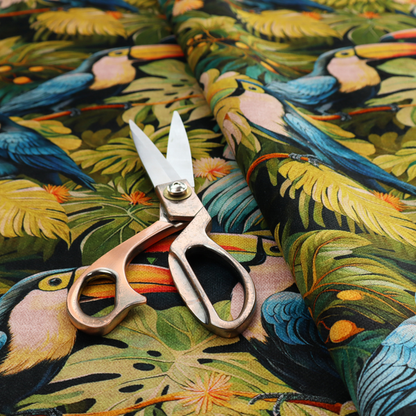 Tropical fabric featuring a repeating pattern of blue toucans perched among lush monstera leaves, palm fronds, and yellow flowers.   