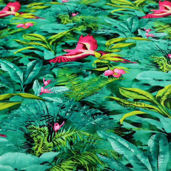 Tropical fabric featuring vibrant magenta parrots in flight surrounded by lush green palm fronds, banana leaves, and pink tropical flowers.   