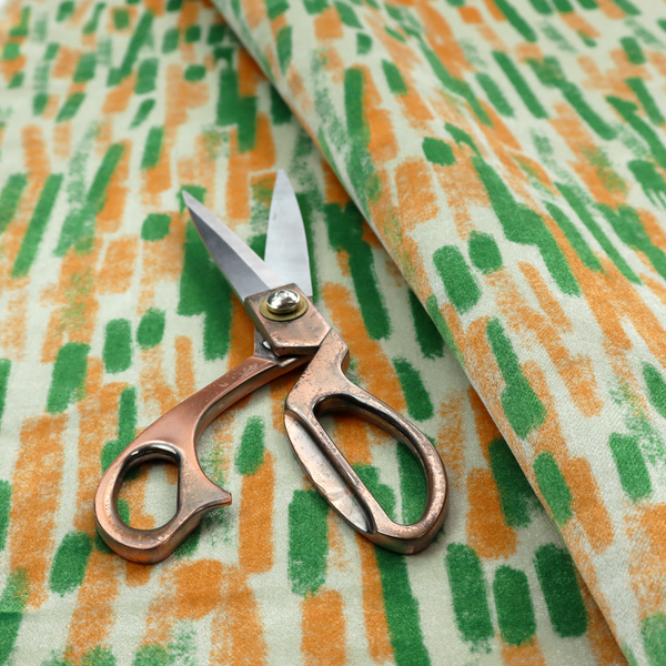 A textured abstract pattern featuring vertical brushstrokes or chalk-like marks in shades of vibrant orange and green against a light off-white or cream background.   