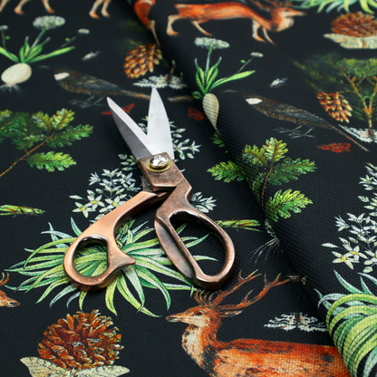 Symmetrical woodland fabric pattern featuring reddish-brown stags with antlers, pinecones, birds, nests with eggs, and botanical flora on a black background.   
