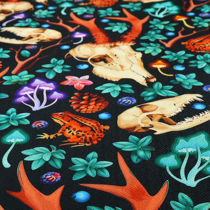 Gothic forest fabric featuring animal skulls with red antlers, bright orange toads, colourful mushrooms, berries, and green foliage on a black background.   