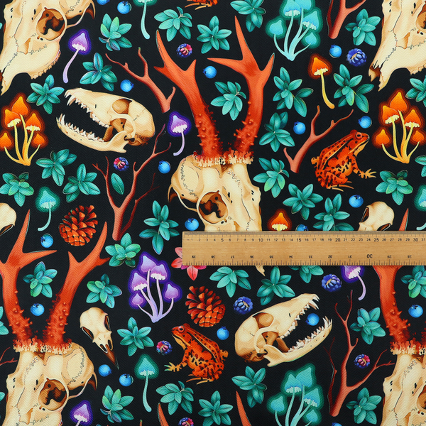 Gothic forest fabric featuring animal skulls with red antlers, bright orange toads, colourful mushrooms, berries, and green foliage on a black background.   