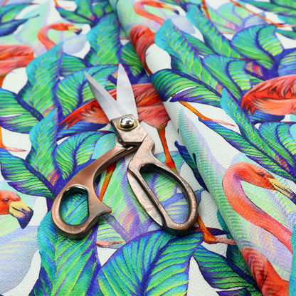 Vibrant tropical fabric pattern featuring coral-pink flamingos nestled among lush green, teal, and blue palm foliage against a white background.   