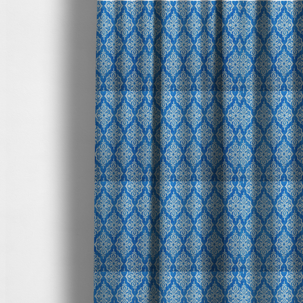 The fabric used to create these made-to-measure curtains is a vibrant royal blue woven fabric featuring an ornate, repeating white damask medallion pattern with a textured ikat effect.   