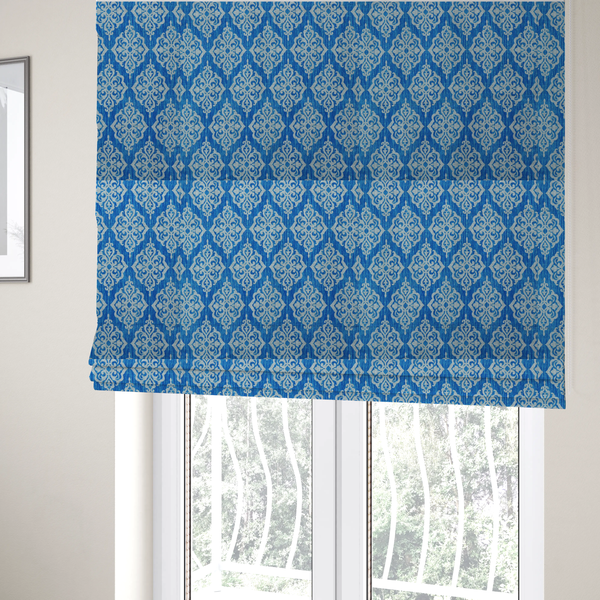 The fabric used to create these Roman blinds is a vibrant royal blue woven fabric featuring an ornate, repeating white damask medallion pattern with a textured ikat effect.   
