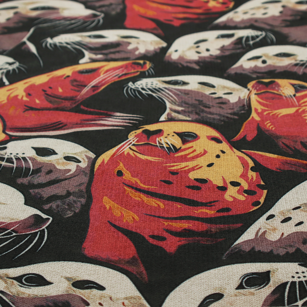 Fabric print featuring a repeating pattern of seals and sea lions in shades of cream, ochre yellow, and coral red on a dark charcoal background.   