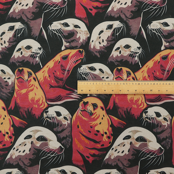 Fabric print featuring a repeating pattern of seals and sea lions in shades of cream, ochre yellow, and coral red on a dark charcoal background.   