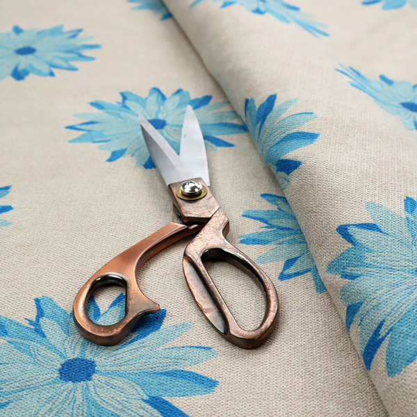 Fabric pattern featuring repeating bright blue daisy-like flowers set against a neutral beige woven background.   