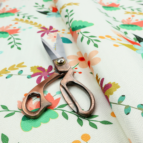 Playful floral fabric featuring scattered colourful bouquets with light blue, coral, purple, and peach blossoms among green stems and mustard foliage on a off-white background.   