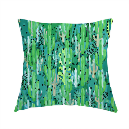 The fabric used to create this handmade cushion is a vibrant, dense pattern of stylized painted saguaro cacti and succulents in shades of green, mint, and white with black polka dots and dashes over a turquoise background.