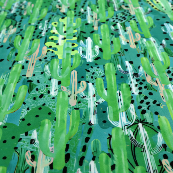 Vibrant, dense pattern of stylized painted saguaro cacti and succulents in shades of green, mint, and white with black polka dots and dashes over a turquoise background.