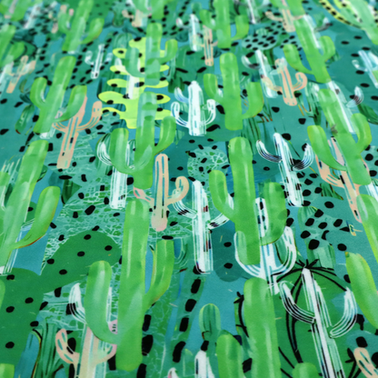 Vibrant, dense pattern of stylized painted saguaro cacti and succulents in shades of green, mint, and white with black polka dots and dashes over a turquoise background.
