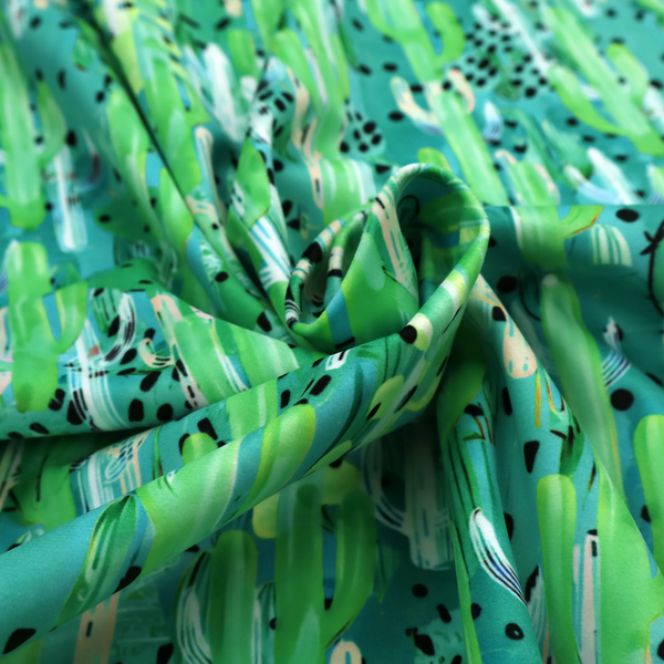 Vibrant, dense pattern of stylized painted saguaro cacti and succulents in shades of green, mint, and white with black polka dots and dashes over a turquoise background.