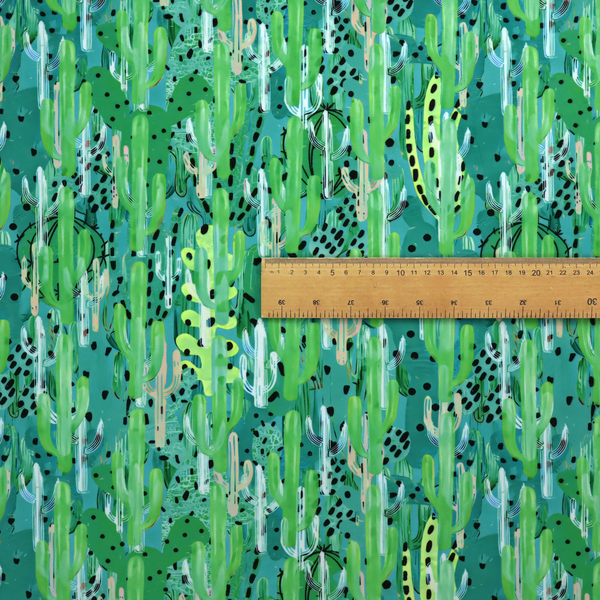 Vibrant, dense pattern of stylized painted saguaro cacti and succulents in shades of green, mint, and white with black polka dots and dashes over a turquoise background.