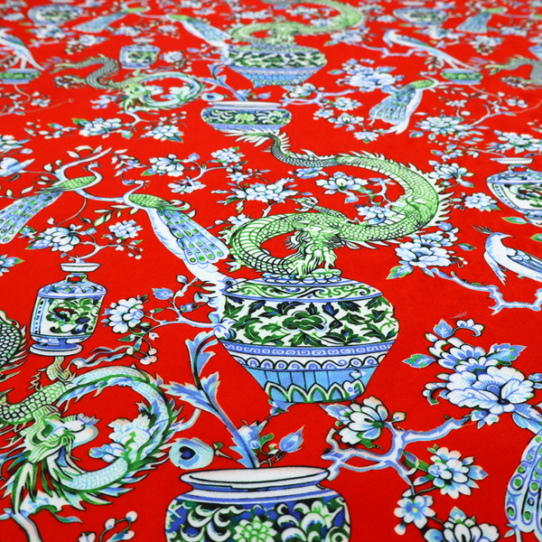Vibrant red Chinoiseries fabric featuring an intricate pattern of green dragons, elegant peacocks, blue-and-white porcelain vases, and blossoming floral branches.