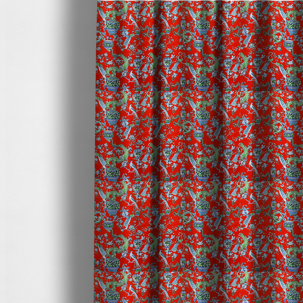 The fabric used to create these made-to-measure curtains is a vibrant red Chinoiseries fabric featuring an intricate pattern of green dragons, elegant peacocks, blue-and-white porcelain vases, and blossoming floral branches.