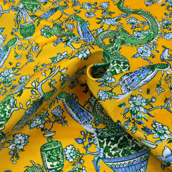 Seamless fabric pattern featuring Chinoiserie-style green dragons, blue and white peacocks, ornate vases, and floral branches against a vibrant mustard yellow background.