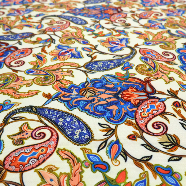 Cream-coloured fabric with an ornate repeating paisley pattern showcasing royal blue tear-drop motifs, vibrant coral and orange florals, and flowing leafy vines.   